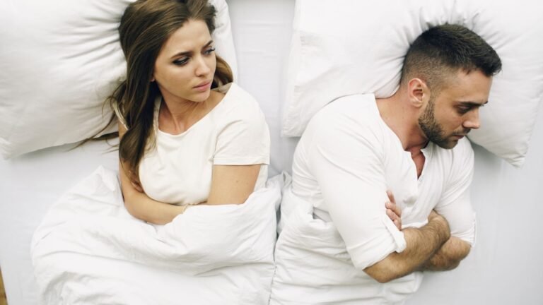 Casal deitado na cama, de costas um para o outro
