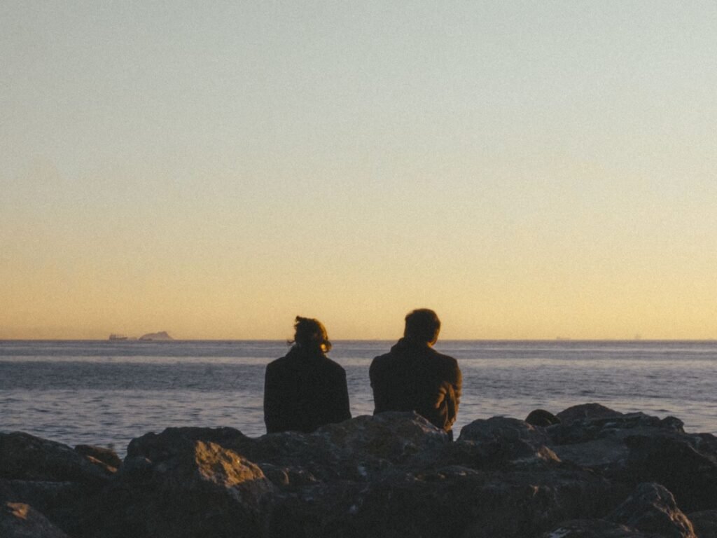Casal sentado nas pedras, olhando o pôr do sol